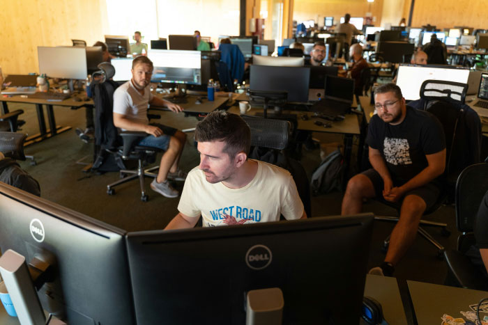 Group of young professionals working on computers in an open office, illustrating AI industry behind-the-scenes environment.