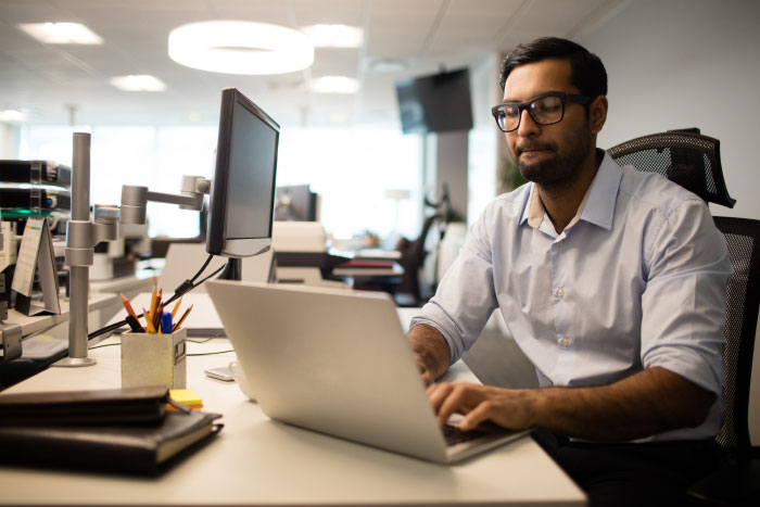 Man in glasses working on laptop in office, focused on AI industry insights and technology development tasks.
