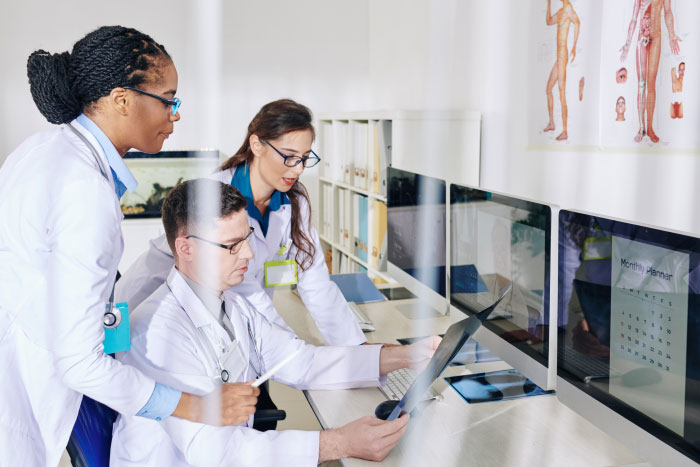 Three doctors reviewing medical images on a tablet and computer screens, highlighting AI industry insights in healthcare.