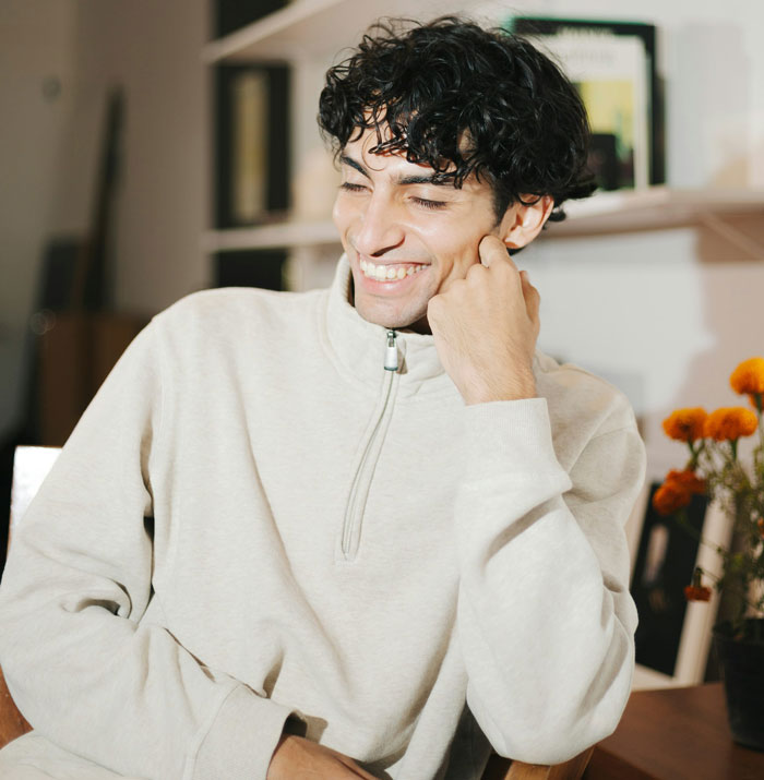 Young secretly gay teen smiling confidently indoors, teaching homophobic parents a lesson on respect in his own way.