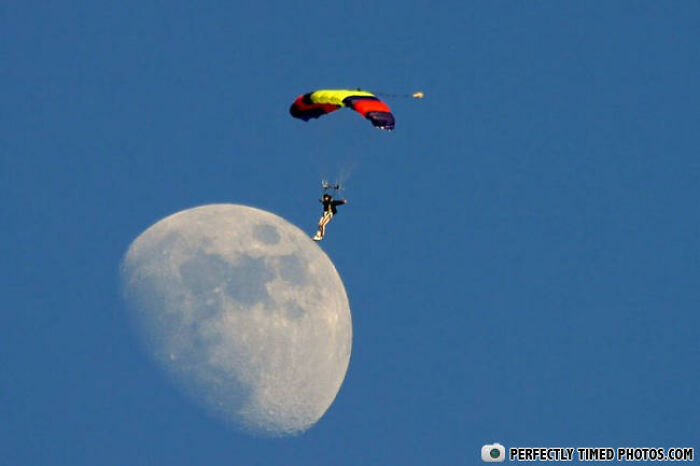 Skydiver with a colorful parachute captured in a perfectly timed photo against a large moon backdrop.