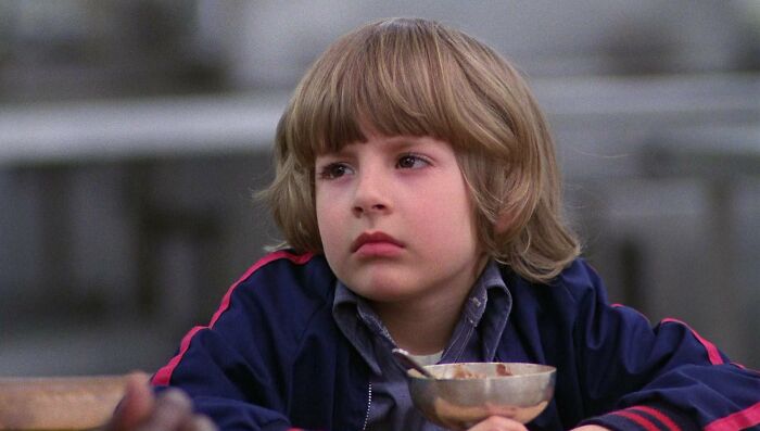 Young boy in a blue jacket looking thoughtful while holding a bowl, reflecting on a once-famous regular job.