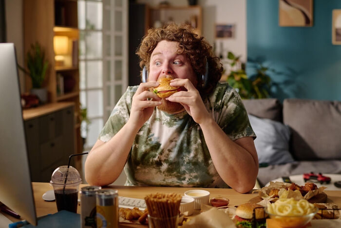 Young man eating fast food at a cluttered table, highlighting overrated and overpriced experiences with popular meals.