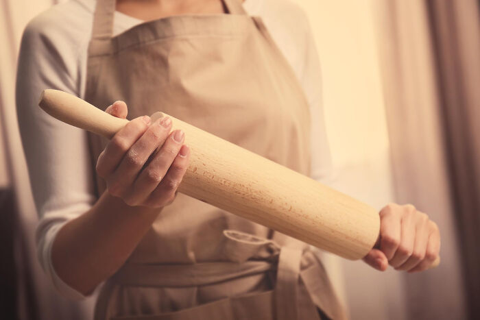 Person wearing an apron holding a wooden rolling pin preparing for a cooking experience often seen as overrated or overpriced.