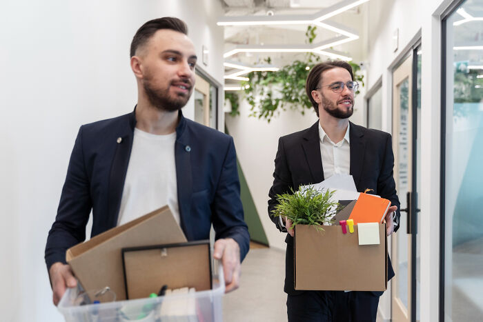 Two men in office attire carrying boxes with belongings, illustrating overrated or overpriced experiences at work.
