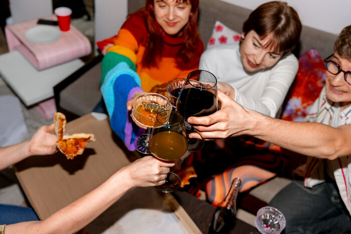 Group of friends toasting with drinks and eating pizza, highlighting overrated and overpriced experiences.