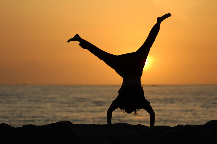 Silhouette of person doing a handstand on rocks by the ocean at sunset, illustrating overrated experiences outdoors.