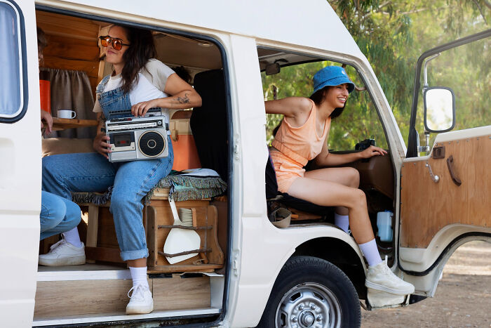 Two women enjoying a road trip in a campervan, highlighting must-try experiences that can be overrated or overpriced.