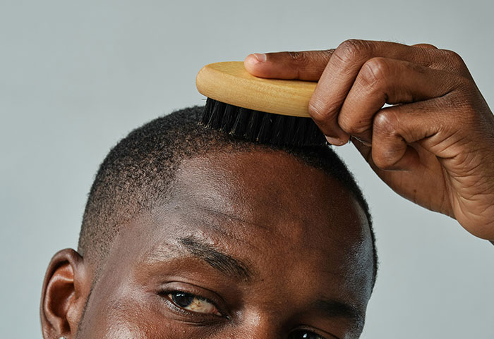 Close-up of a man grooming his hair with a brush, illustrating female roasts that hit men hard and leave an impact.