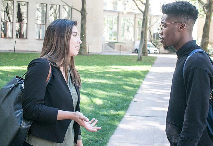 A woman delivering a sharp female roast to a man outdoors in a casual conversation on a sunny day.