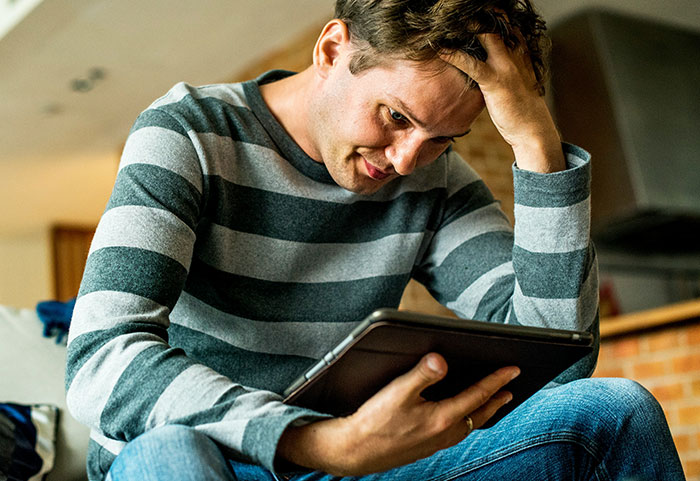 Man in striped shirt looking stressed while holding a tablet, reflecting on female roasts hitting men hard.