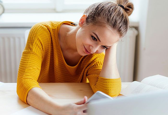 Woman in a yellow sweater looking at phone with a smirk, capturing the essence of female roasts hitting men hard.
