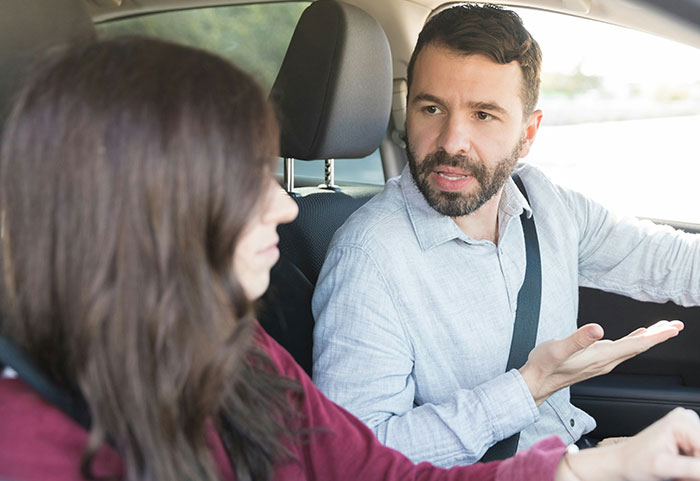 Woman delivering a sharp female roast to a man in a car, capturing intense emotions and strong reactions.