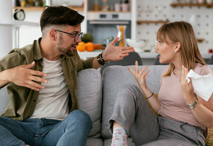Woman delivering powerful female roasts to a man during a heated conversation on a living room couch.
