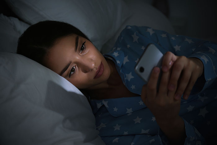 Woman in star-patterned pajamas lying in bed at night, looking upset while holding a smartphone.