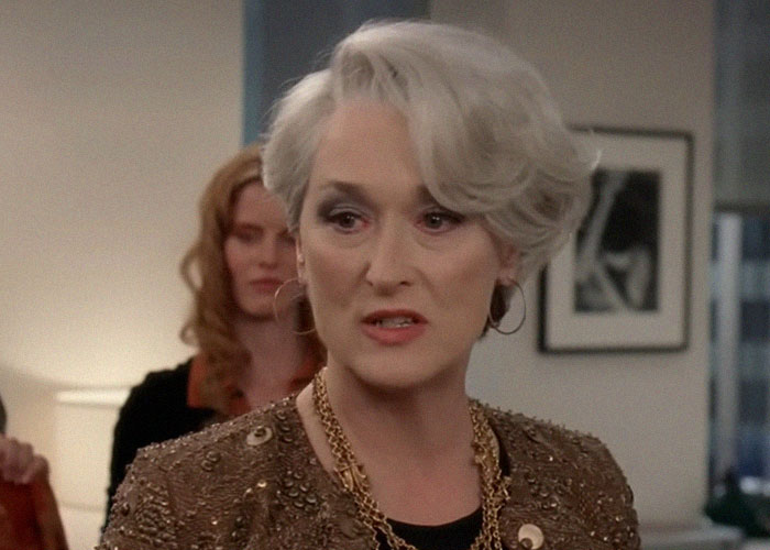 Woman with short silver hair and gold accessories speaking seriously in an office, illustrating interesting today I learned facts.