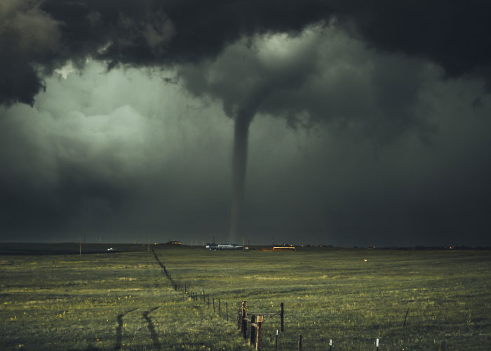 A dark tornado funnel touching down in a flat rural landscape under ominous stormy clouds, dramatic weather scene.