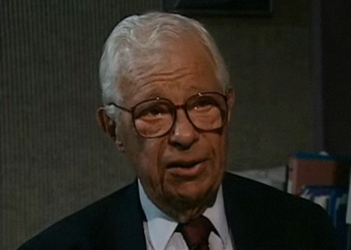 Elderly man wearing glasses and a suit speaking in an indoor setting about interesting today I learned facts.