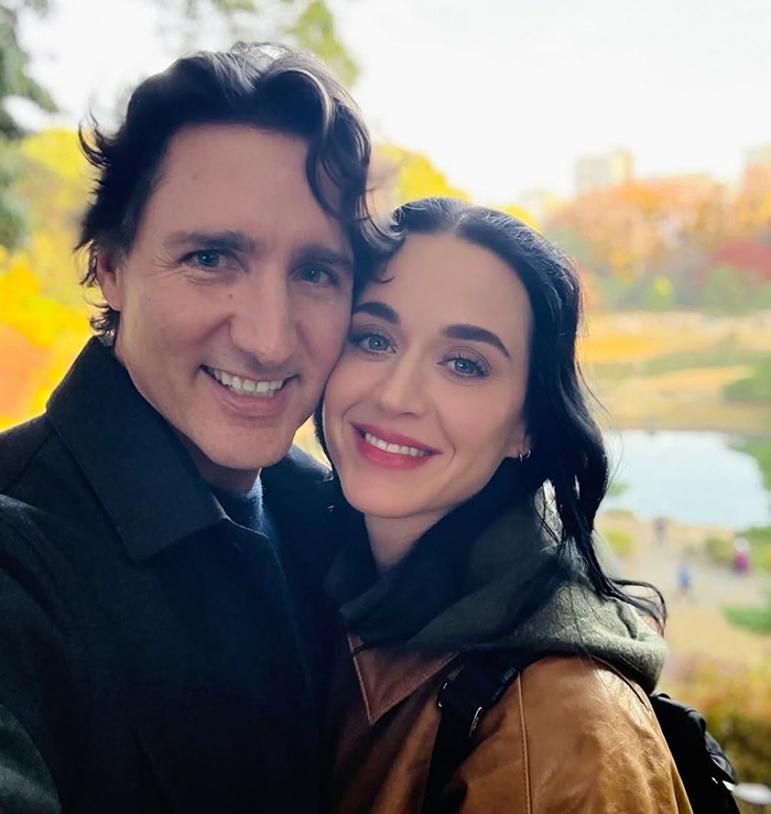 Justin Trudeau and Katy Perry smiling together outdoors, capturing a happy moment amid fall foliage and park scenery.