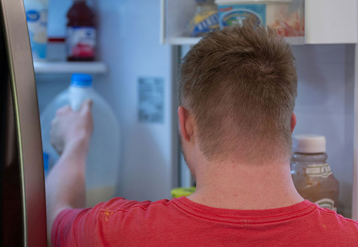 Man in a red shirt grabbing milk from an open fridge illustrating dad privileges from moms' perspectives.