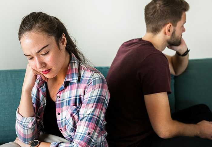 Upset mother and father sitting back to back on couch, highlighting tension and dad privileges in parenting roles.