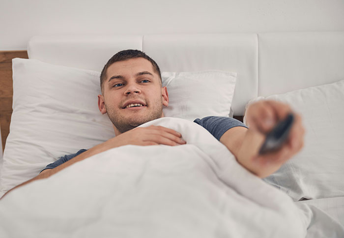 Man lying in bed holding remote control, illustrating dad privileges in a relaxed home setting.