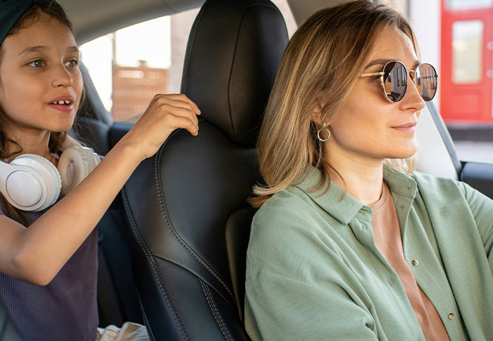 Woman driving car with child in backseat, illustrating challenges moms face compared to dad privileges in parenting.