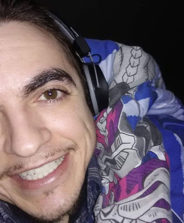 Close-up of Tylor Chase smiling warmly while wearing headphones and wrapped in a colorful blanket, related to hospitalization news.