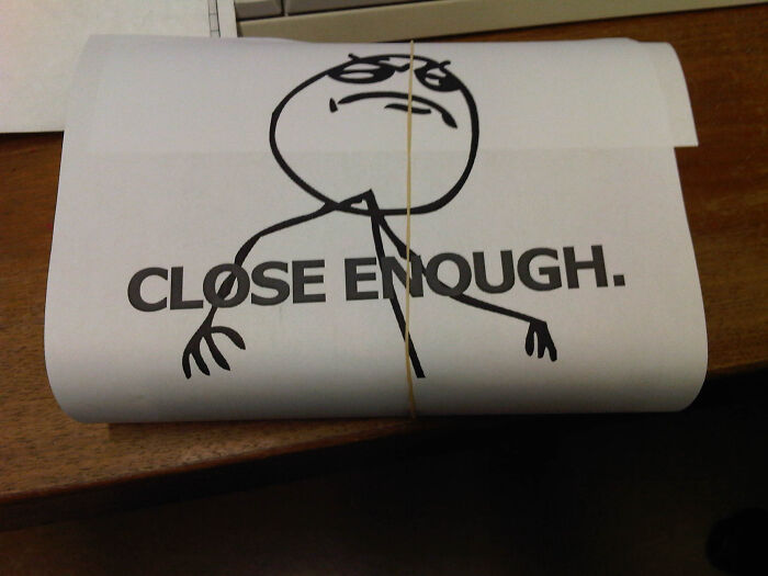 Rolled funny gift wrap featuring a meme face with text close enough, tied with a rubber band on a wooden surface.