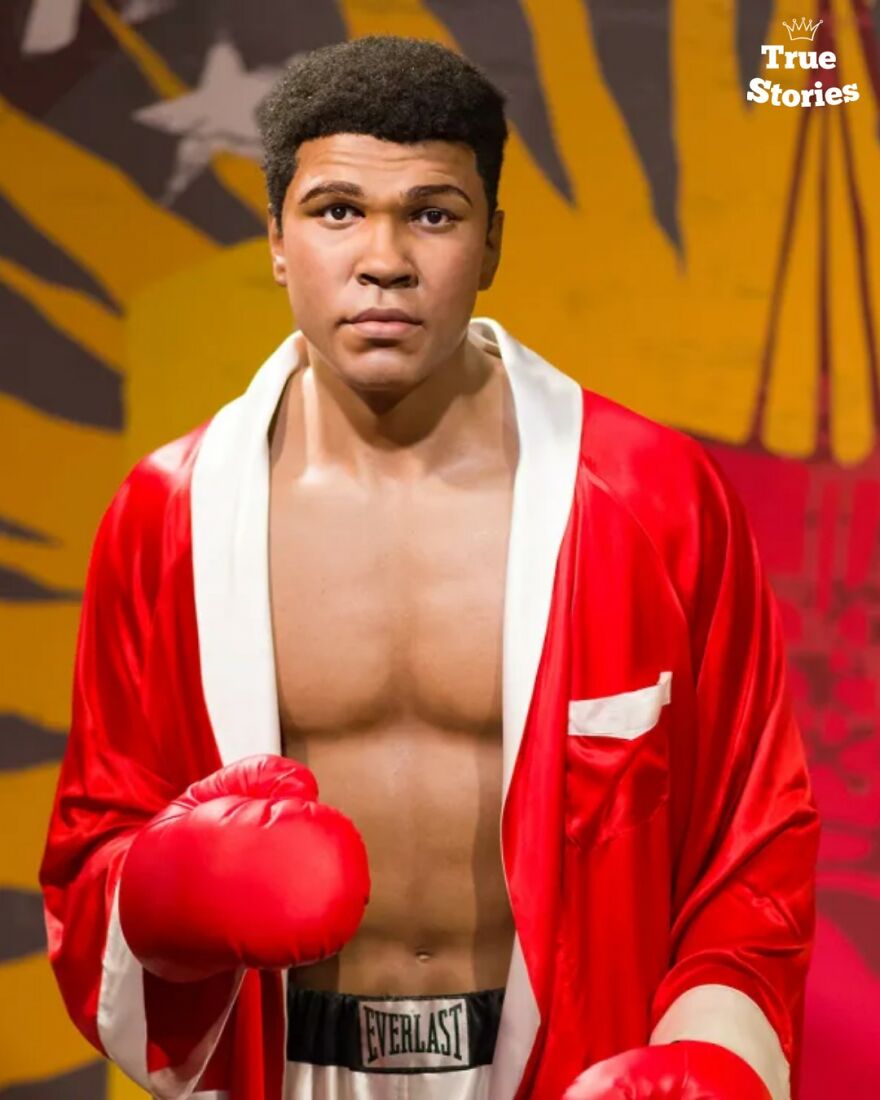 Wax figure of an important American personality wearing red boxing gloves and a red robe in a museum setting.