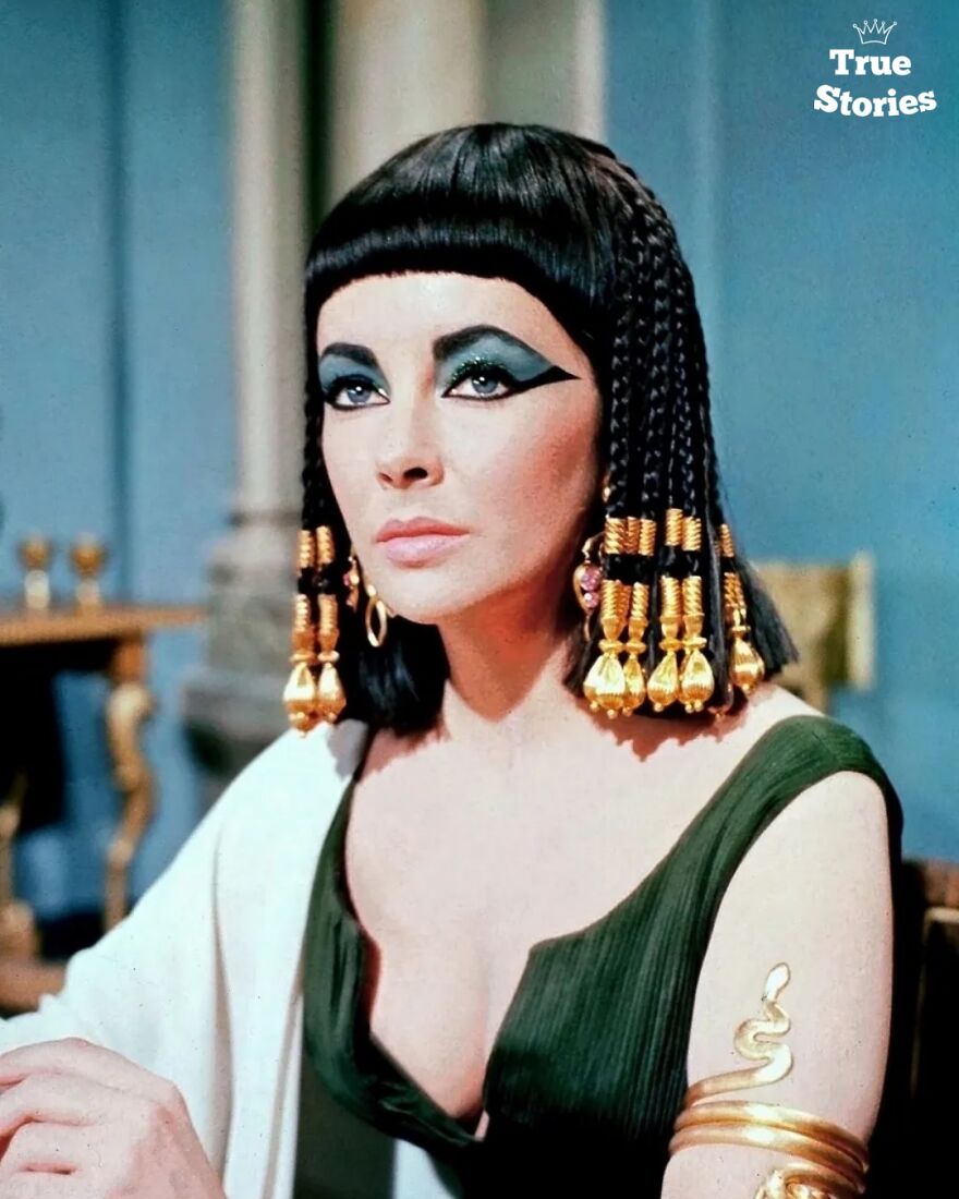 Actor in Cleopatra costume with Egyptian style makeup and gold jewelry, representing important American personalities.