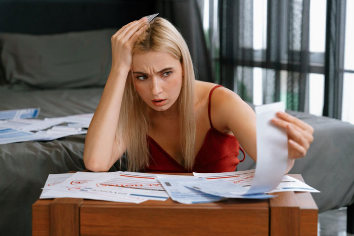 Woman stressed about bills, sitting at table surrounded by paperwork, struggling with unemployed husband pay bills situation.