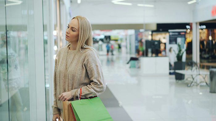Woman shopping in mall looking thoughtful and holding bags, reflecting on SAHM financial challenges and fun money budget.