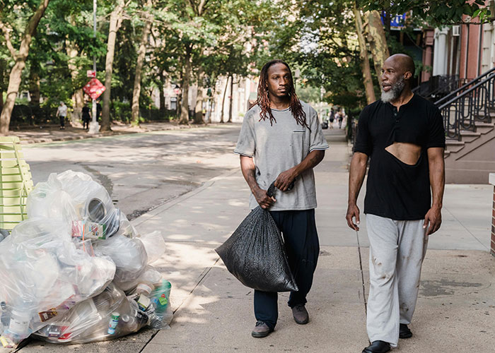 Two men walking on a sidewalk near trash bags, depicting a scene from stranger things people accidentally saw neighbors doing.