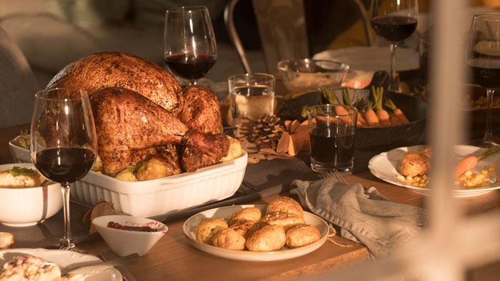 Thanksgiving dinner table with roasted turkey, red wine glasses, and traditional side dishes in a cozy setting. Thanksgiving dinner table with roasted turkey, red wine glasses, and traditional side dishes in a cozy setting.