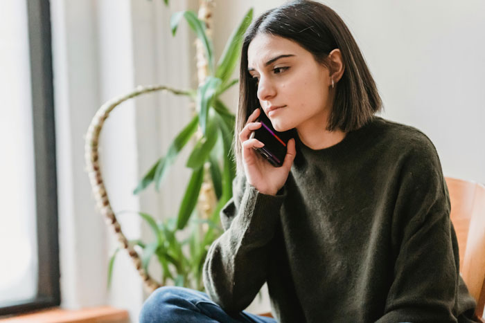 Young woman in a green sweater talking on phone indoors, representing babysitting and gym balance challenges for couples.