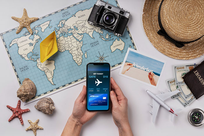 Hands holding phone with digital boarding pass near travel map, camera, hat, and toy airplane symbolizing Hawaii trip plans canceled.