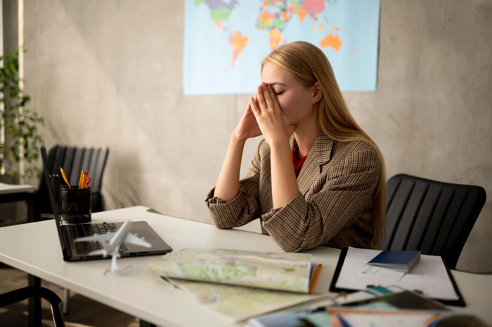 Young woman stressed at desk with travel map and laptop, reflecting tension from canceled Hawaii trip conflict
