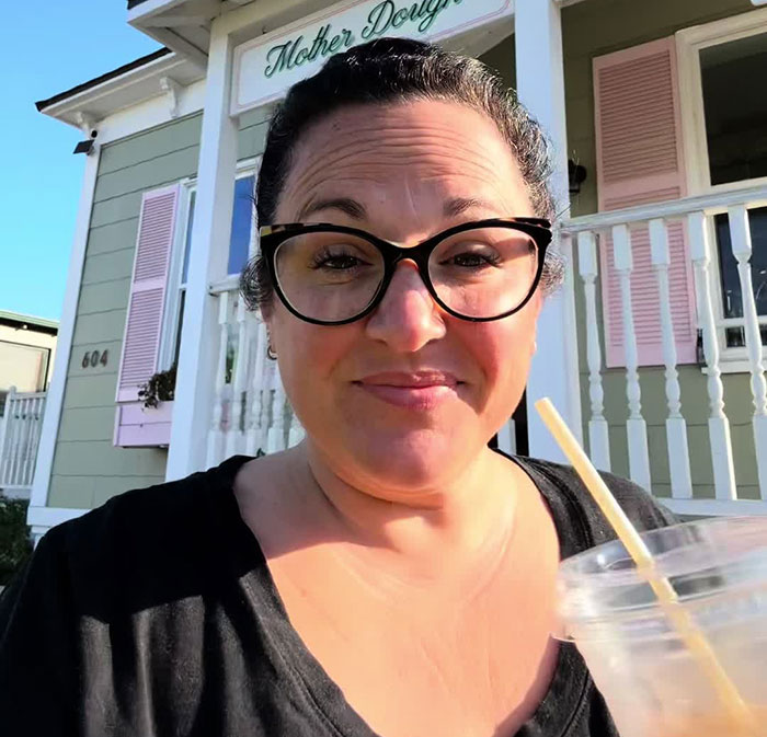 Woman with glasses holding drink, reacting emotionally after catching glimpse of seatmate's body-shaming text on flight.
