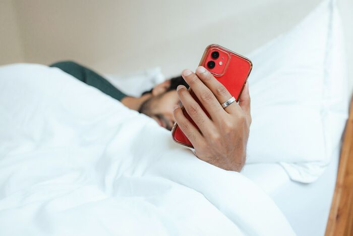 Person lying in bed holding a red phone, illustrating common harmless but toxic habits affecting daily life.