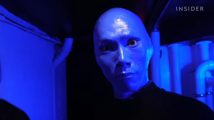 Person wearing a blue mask with a blank expression in a dimly lit room, showcasing secrets about celebrities revealed.