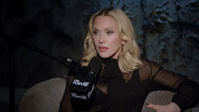 Celebrity sitting in a dark room, speaking into a microphone during a podcast about celebrities people think suffer.