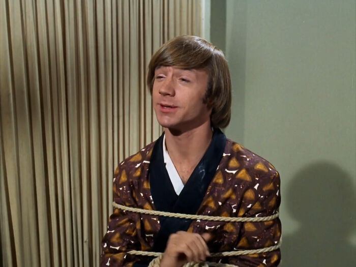 Young man wearing a patterned robe tied with rope against a wall, illustrating once-famous regular job concept.