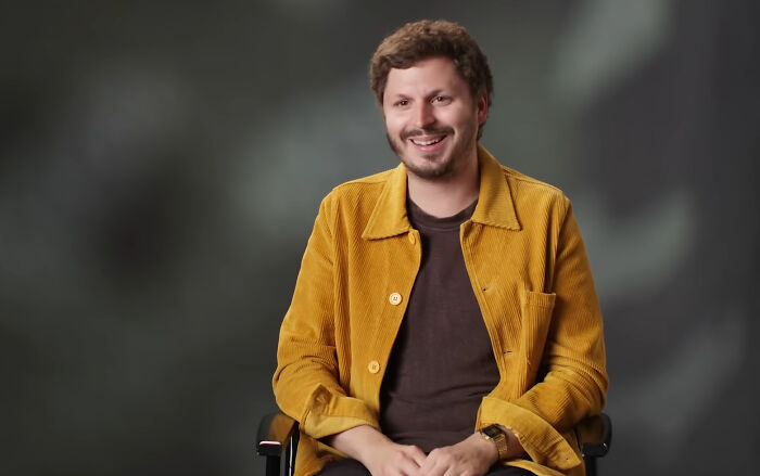 Man in a mustard jacket sitting and smiling in an interview setting sharing fascinating secrets about celebrities.