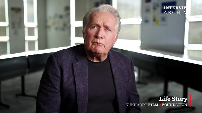 Older man in a dark blazer sharing fascinating secrets about celebrities in a bright, modern interview setting.