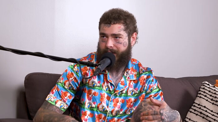 Post Malone speaking into a microphone during an interview about celebrities people think suffer, wearing a colorful shirt.