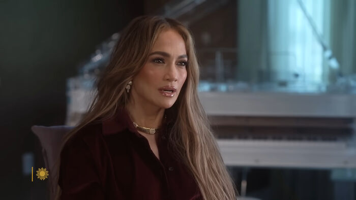 Female celebrity in a dark outfit, seated indoors near a white piano, reflecting on people think celebrities closet skeletons.