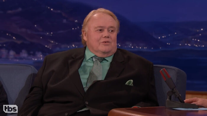 Comedian in a black suit and green shirt sharing fascinating secrets about celebrities on a late-night talk show.