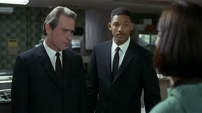 Two men in black suits and ties talk to a woman, portraying a once-famous regular job in a professional setting.