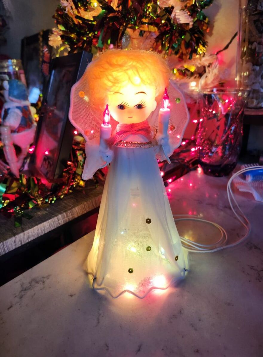 Vintage Christmas decoration of a glowing angel figurine holding two candles on a festive background.